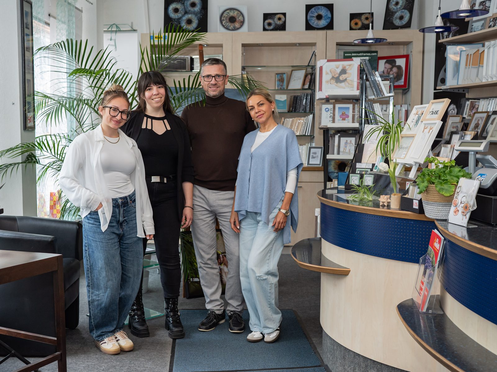 Viktor Obholz mit einem Fotostudio-Team im Ladengeschäft des Studios, im Hintergrund Bilderrahmen und der Empfangstresen